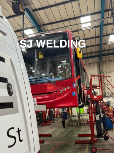 Red bus in a workshop, elevated on a lift with tools and equipment around.