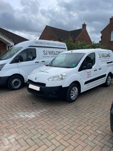 Two white vans parked in a residential driveway under a cloudy sky.