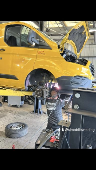 A mechanic working on the engine of a yellow van in a garage.